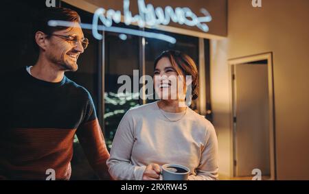 Glücklicher Mann und glückliche Frau, die zusammen an einer Glaswand stehen, in der Nacht ein Brainstorming durchführen und an einem Geschäftsprojekt mitarbeiten. Zwei Unternehmer, die sich einmischen Stockfoto