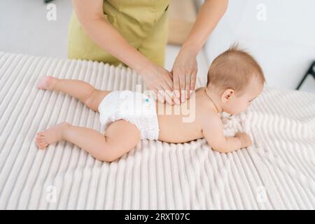 Blick auf liebevolle Mutterhände, die das kleine Baby massieren. Nahaufnahme eines abgeschnittenen Schusses von unbekannten Händen der Masseurin, die das Neugeborene massieren. Stockfoto