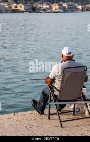 Älterer Rentner sitzt an einer Hafenmauer und fischt in der warmen Sommersonne. Stockfoto