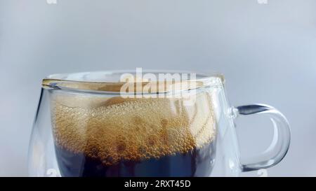 Nahaufnahme von schwarzem Kaffee mit Naturschaum in doppelwandigem transparentem Glas mit einfachem Hintergrund, Morgenboost, Espresso, Americano, dunkel geröstet, RO Stockfoto