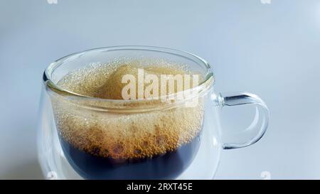 Nahaufnahme von schwarzem Kaffee mit Naturschaum in doppelwandigem transparentem Glas mit einfachem Hintergrund, Morgenboost, Espresso, Americano, dunkel geröstet, RO Stockfoto
