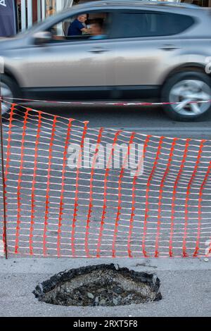 Auto, das an einem großen und tiefen Schlagloch auf dem Asphalt auf einer von den örtlichen Behörden gepflegten Autobahn oder Straße vorbeifährt. Stockfoto