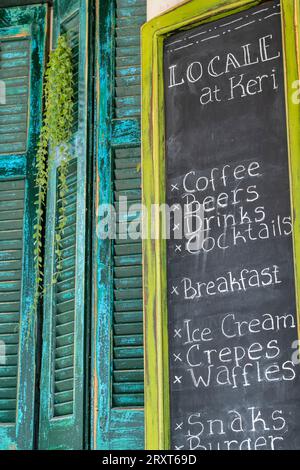 Menü-Board vor einem griechischen Restaurant oder einer Taverne mit rustikalen, schäbigen, schicken Fensterläden in blätternder Blau- und Grünfarbe. Stockfoto