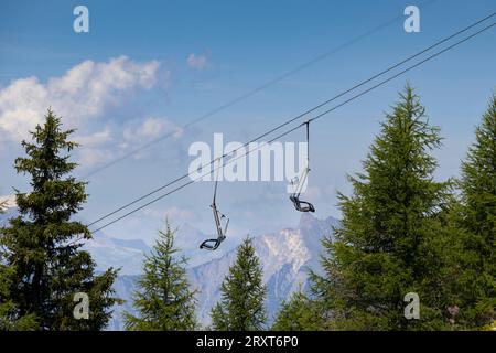 Ein leerer Sessellift im Sommer, über dem Wald, mit Bergen im Hintergrund. Skigebiet La Fouly in der Schweiz. Leerzeichen darüber kopieren. Stockfoto