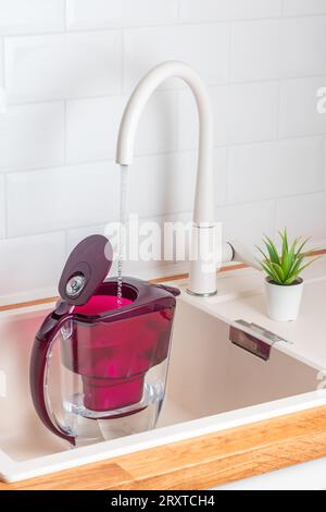 Gießen von Wasser aus der Küchenleitung in eine Wasserfilterkanne, Dose mit alkalischen Filtern Stockfoto