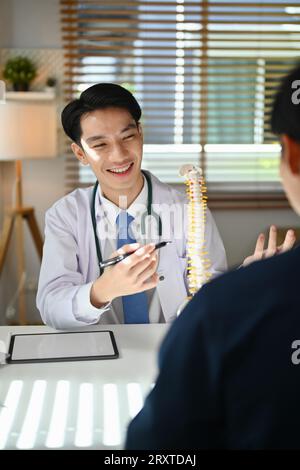 Orthopäde in weißer medizinischer Laborkittel, die dem Patienten das Problem am Wirbelsäulenmodell demonstriert. Gesundheitskonzept Stockfoto