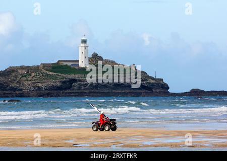 Rettungsschwimmer auf einem Quad mit der Sicherheitsfahne bei Ebbe, Godrevy Sands, Godrevy Island und Leuchtturm mit Atlantik Surf, Nr. Hayle, Cornwall, Großbritannien Stockfoto