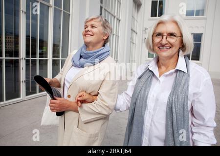 Lifestyle Porträt freudige ältere Frauen mit grauen Haaren, die gemeinsam durch die Stadt gehen, vorbei an einem wunderschönen Gebäude. Seniorinnen teilen sich s Stockfoto