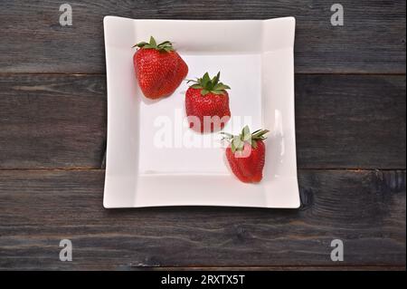 Drei Erdbeeren auf einem weißen Teller auf einem hölzernen Hintergrund. Konzept Stockfoto