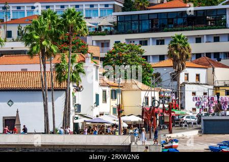 Malerischer Blick auf das kleine Fischerdorf Câmara de Lobos in Madeira, Portugal, wo Touristen das Hafenleben an der Uferpromenade genießen Stockfoto