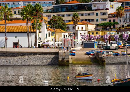 Malerischer Blick auf das kleine Fischerdorf Câmara de Lobos in Madeira, Portugal, wo Touristen das Hafenleben an der Uferpromenade genießen Stockfoto