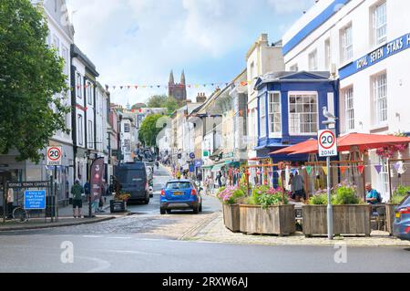 Blick auf die Fore Street im Stadtzentrum von Totnes mit unabhängigen Geschäften und Cafés und St Mary's Parish Church, South Hams, South Devon, England, Großbritannien Stockfoto
