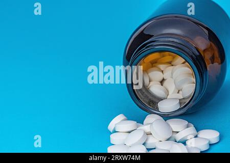 Weiße runde Pillen aus einer braunen Flasche auf blauem Hintergrund gestreut. Thema Pharmazie und Gesundheitswesen. Medizinischer Hintergrund, Kopierbereich. Suchtbehandlung Stockfoto