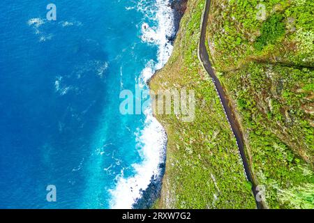 Wunderschöner Blick aus der Vogelperspektive auf eine Klippenstraße in Madeira, Portugal, hoch über dem Meer entlang des Hanges und tief unter den Wellen krachen die Felsen Stockfoto