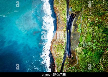 Wunderschöner und atemberaubender Blick aus der Vogelperspektive auf ein gelbes Auto, das zwischen zwei Tunneln auf einer Klippenstraße in Madeira, Portugal, fährt Stockfoto