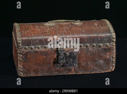 Geldbox, die dem Gründer der African Methodist Episcopal (AME) Church, Bischof Richard Allen, gehörte. Das rechteckige Kästchen ist auf allen Seiten flach mit einem flachen Boden. Es hat eine leicht gewölbte Oberseite mit einem horizontalen 1 7/8'-Schlitz in der Mitte. Der Messinggriff auf der Oberseite ist durch flache runde Scheiben auf beiden Seiten des Schlitzes mit dem Gehäuse verbunden. Die Oberseite der Box ist ein aufklappbarer Deckel, der hinten mit zwei Scharnieren befestigt ist. Die Box besteht aus Holz und ist mit dunklem, rötlich-braunem Leder bedeckt. An der Vorderseite der Box ist ein Metallverriegelungsmechanismus mit einem klappbaren Teil angebracht, das in eine Zeitlupe passt Stockfoto