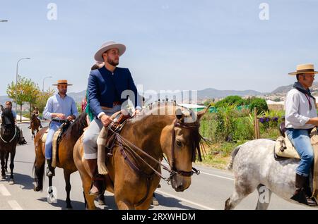 NERJA, SPANIEN - 15. MAI 2022 Frauen in Flamenco-Kleidern und Männer auf andalusischen Pferden in ihren besten traditionellen Volkstrachten und breitkrempigen Mützen Stockfoto