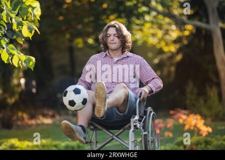 Junger Rollstuhlsitzender Mann mit Rehabilitationsprogramm nach Verletzung und Training mit Fußball Stockfoto