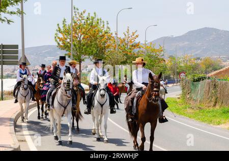 NERJA, SPANIEN - 15. MAI 2022 Frauen in Flamenco-Kleidern und Männer auf andalusischen Pferden in ihren besten traditionellen Volkstrachten und breitkrempigen Mützen Stockfoto