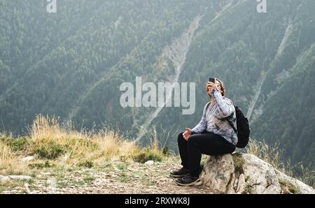 Junger Mann macht Fotos auf seinem Handy bei einer Pause während einer Wanderung in den Bergen, aktive Erholung Stockfoto