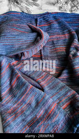 Handgefertigte Strickwaren. Strickjacke aus violetten und roten Fäden. Grauer Hintergrund. Leerzeichen kopieren Stockfoto