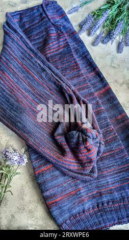 Handgefertigte Strickwaren. Strickjacke aus violetten und roten Fäden. Grauer Hintergrund. Leerzeichen kopieren Stockfoto