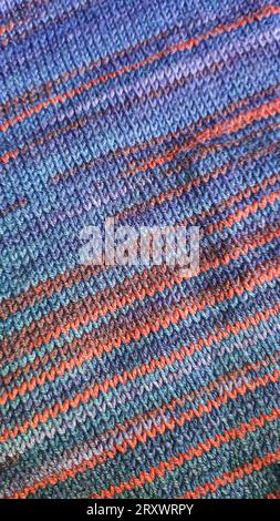 Handgefertigte Strickwaren. Strickjacke aus violetten und roten Fäden. Grauer Hintergrund. Leerzeichen kopieren Stockfoto