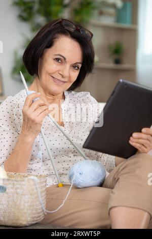 Seniorinnen sehen sich Online-Serien auf elektronischen Geräten und Stricken an Stockfoto