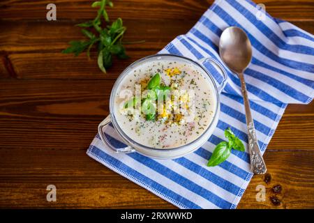 Kalte Suppe mit Gurken, Eiern, Gemüse, Joghurt und frischen Kräutern in einer Glasschale auf einem Holztisch. Stockfoto