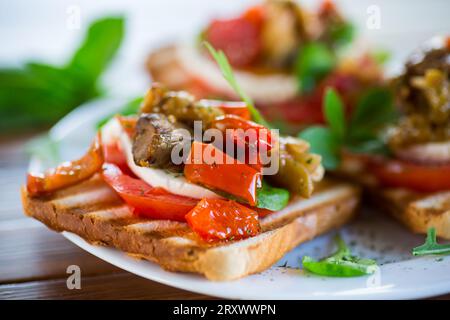 Zubereitetes Sandwich mit Tomaten, Mozzarella und frittierter Aubergine mit Pilzen auf einem Teller auf einem Holztisch. Stockfoto