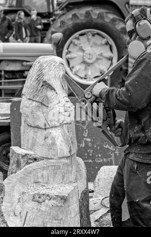 Männlicher Bildhauer bei der Nidderdale Show mit Kopfhörern und einer Gesichtsmaske, mit der eine Kettensäge eine Eule aus Holz schnitzt, Pateley Bridge, Yorkshire, UK. Stockfoto