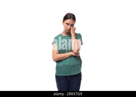 30 Jahre alte schlanke, brünette Frau mit Pferdeschwanz-Frisur in einem grünen T-Shirt hat Zweifel Stockfoto