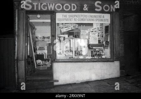 1960er Jahre, historisch, Außenansicht des Stigwood & Son Stores, Schaufensterbanner mit der Aufschrift „The Shopkeepers Engineers & Equipment Re-Conditioning Specialists, Oldham, England, Großbritannien. Die Fensteranzeige enthält Schallplatten, Plattendecks, Funkgeräte + Poster Abour Waagen, Gewichtungsmaschinen und Slicer. Stockfoto