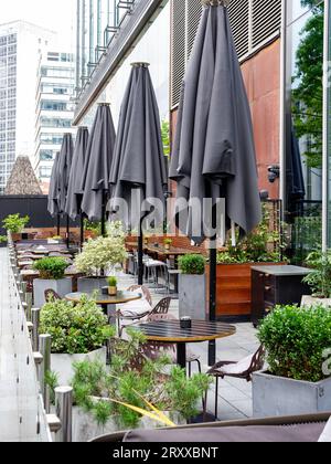 Eine Reihe von Sonnenschirmen in einem Restaurant im Freien in der Stadt mit Tischen und Stühlen gefaltet Stockfoto