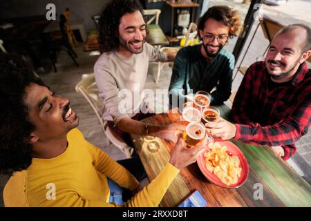 Vier glückliche männliche Freunde toasten mit Bier in einer Bar, haben Spaß und genießen den Abend zusammen. Stockfoto