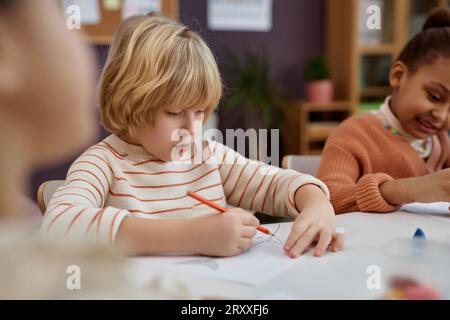 Porträt von niedlichen blonden Jungen, die Bilder am Tisch in Kunst- und Handwerkskurs im Vorschulalter, Kopierraum ausmalen Stockfoto