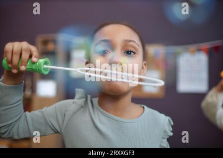 Porträt eines süßen Schwarzen Mädchens, das mit Seifenblasen im Vorschulalter spielt und die Kamera anschaut Stockfoto