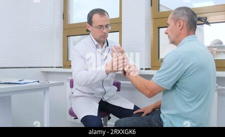 Der Arzt untersucht die Schmerzen des Handgelenks bei einem älteren Patienten. Stockfoto