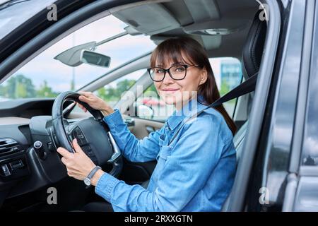 Eine Fahrerin mittleren Alters sitzt im Auto hinter dem Steuer und schaut lächelnd auf die Kamera Stockfoto