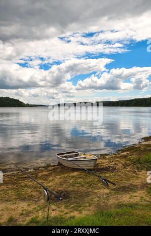 Tagsüber Urlaubslandschaft am Wasser. Boot am Ufer des Sees und Wolken spiegeln sich im Wasser. Fotos am Chancza-See, Polen. Stockfoto