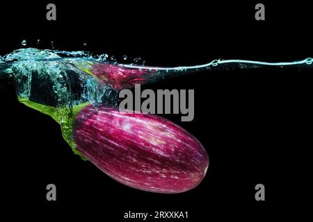 Nahaufnahme einer Graffiti-Aubergine unter Wasser mit Spritzern auf Schwarz. Stockfoto