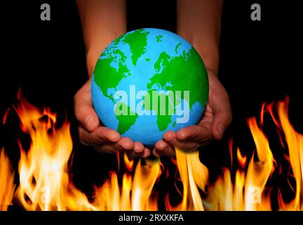 Ein Paar Hände hüllen einen Globus mit üppig grünen Kontinenten vor dem Hintergrund der Flammen. Konzept zur Planetenpflege und zum Schutz. Stockfoto