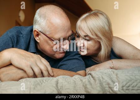 Porträt eines verheirateten älteren Ehepaares, das auf dem Bett liegt und sich anschaut. Stockfoto