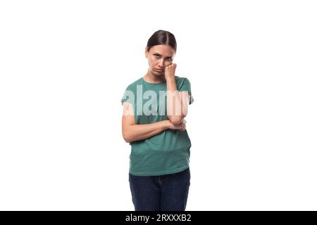 30 Jahre alte schlanke, brünette Frau mit Pferdeschwanz-Frisur in einem grünen T-Shirt hat Zweifel Stockfoto
