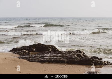 Blick auf Felsen mit Meereswellen an einem Strand, beige, aus der Nähe. Stockfoto