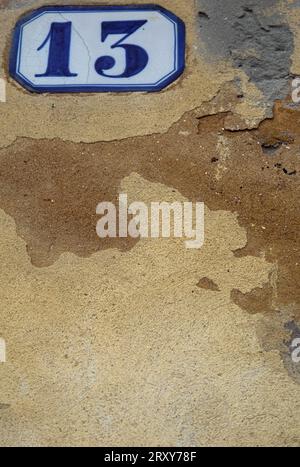 Die Nummer 13, auf einer weißen Tafel mit blauer Einfassung gegen eine gelb-ockerfarbene Wand, schoss nah und füllte den Rahmen. Stockfoto