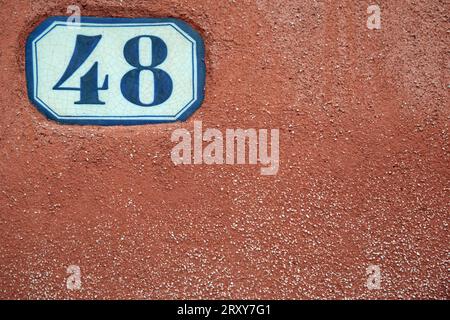 Die Zahl 48 auf einer weißen Keramikplatte, die in das Rendering einer rot lackierten Wand eingelassen ist, nahm Vollbild auf, ließ aber Kopierraum. Stockfoto