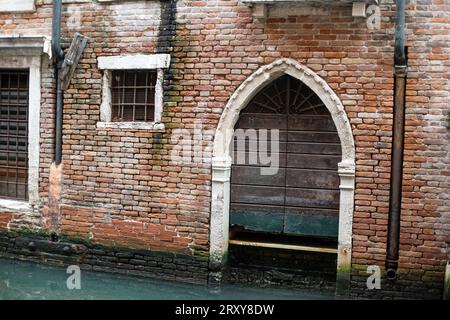 Venedig, Veneto, Italien, 16. September 2023, ein Blick auf eine müde Ziegelmauer, eine bogenförmige Tür und vergitterte Fenster Stockfoto