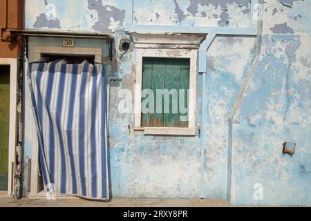 Das Fenster und die Tür sind mit einem gestreiften Vorhang gegen eine verwitterte, blau lackierte Wand verdeckt Stockfoto