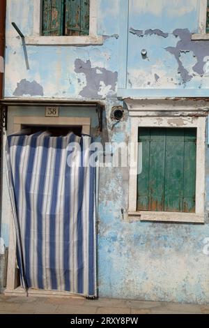 Das Fenster und die Tür sind mit einem gestreiften Vorhang gegen eine verwitterte, blau lackierte Wand verdeckt Stockfoto